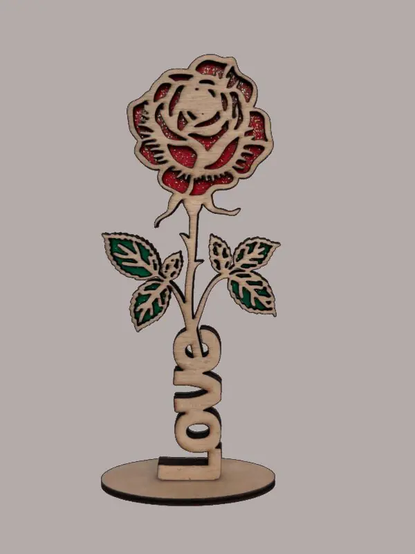 Rose en bois découpée au laser aux pétales rouges pailletés et feuilles vertes, mot Love à la base, posée sur un socle rond