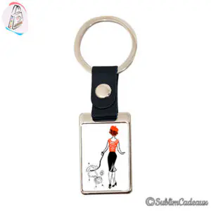 Porte-clés rectangulaire en métal à attache simili cuir noir, illustré d'une femme promenant un caniche
