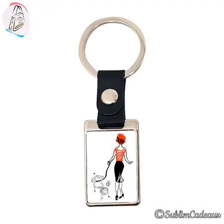 Porte-clés rectangulaire en métal à attache simili cuir noir, illustré d'une femme promenant un caniche