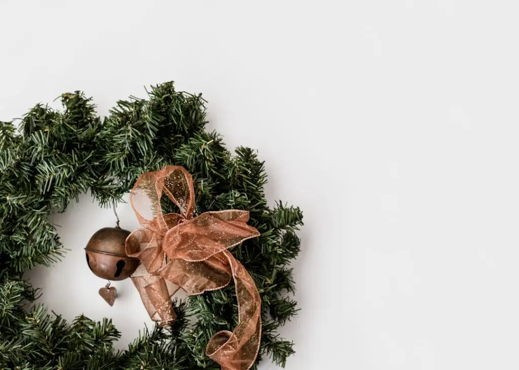 Couronne de Noël en branches de sapin ornée d'un gros grelot doré et d'un nœud en ruban pailleté cuivré, sur fond blanc