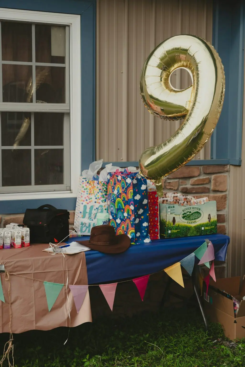 Table de fête d'anniversaire avec un grand ballon doré en forme de chiffre 9, des sacs cadeaux colorés et une guirlande de fanions