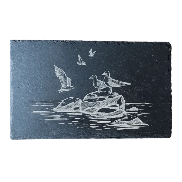 Ardoise noire gravée d'une scène marine avec des mouettes posées sur des rochers et d'autres en vol