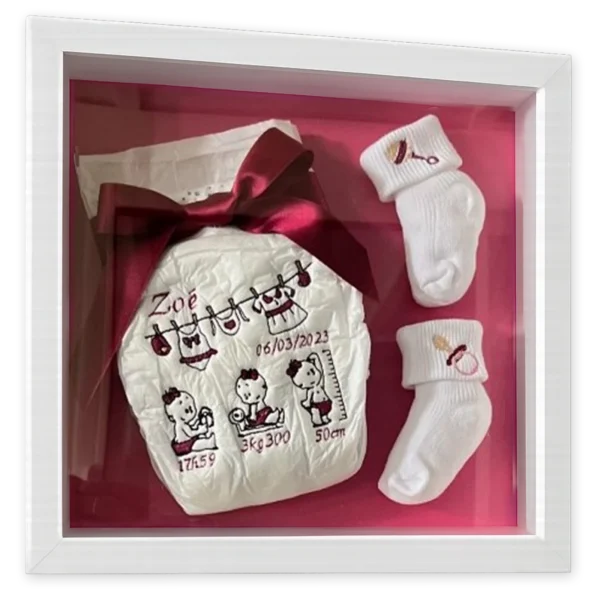 Cadre 3D de naissance avec couche brodée au prénom et aux mesures du bébé et chaussettes blanches, fond rose