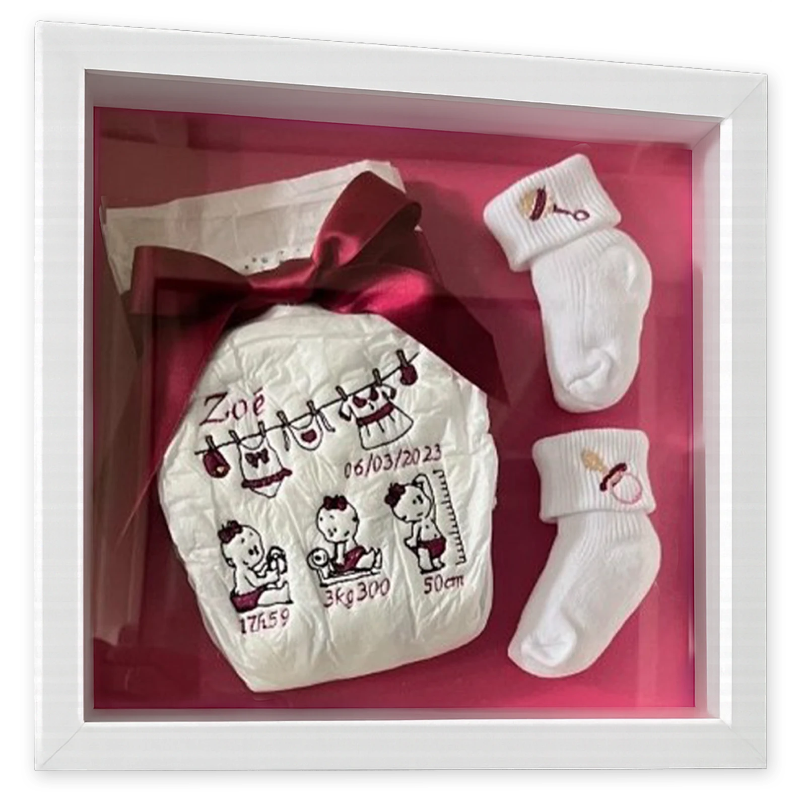 Cadre 3D de naissance avec couche brodée au prénom et aux mesures du bébé et chaussettes blanches, fond rose