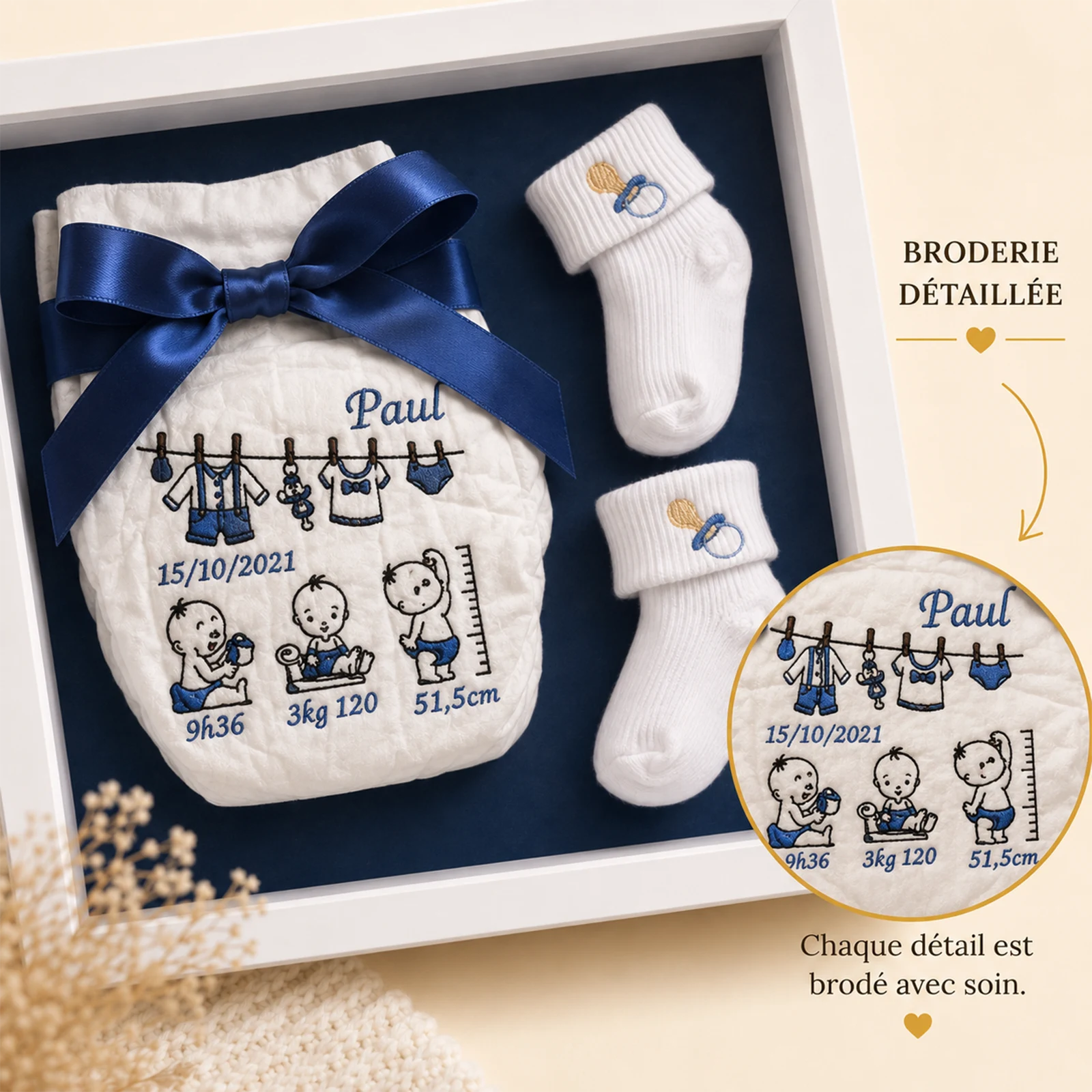 Gros plan de la couche brodée au prénom Paul, date et mesures de naissance en fil bleu marine, chaussons blancs sur fond marine